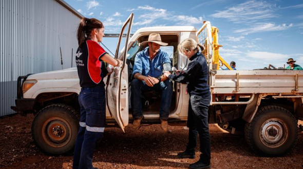 a nurse in an RFDS shirt and a doctor checking the heart rate of a patient who is sitting in a ute