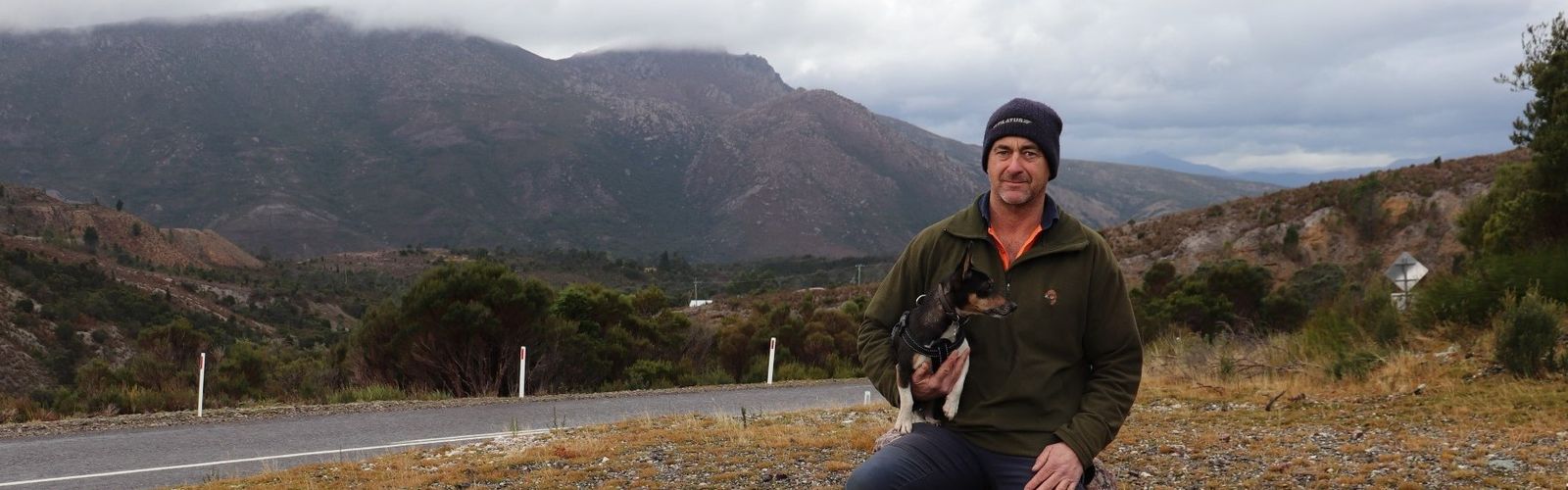 Phil and Digger wait for the RFDS Tasmania Health Hub Bus with Queenstown mountains behind.