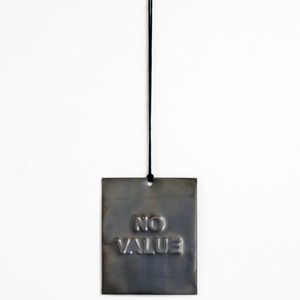 A rectangular dark silver sign with the text "NO VALUE"  is  hanging on a black cord against a white wall