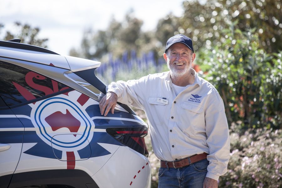 A Community Transport volunteer leaning on a car
