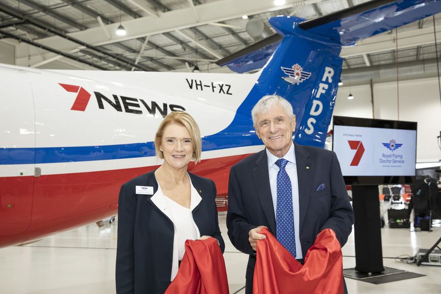 A man and woman stand in front of a RFDS plane with 7 NEWS logo. They are both smiling. 