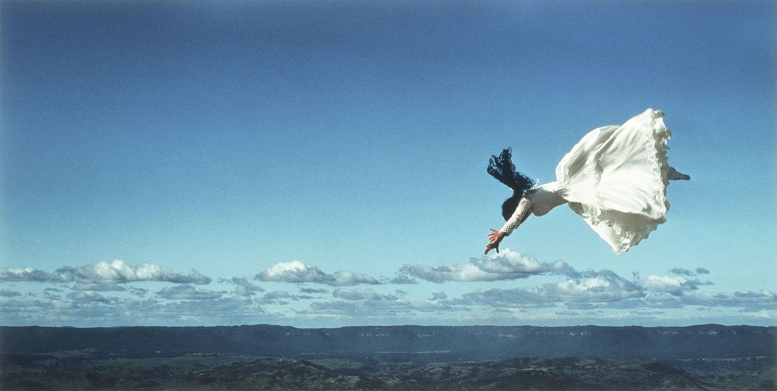 Photo of a woman in a wedding dress diving through the air with a valley landscape in the background