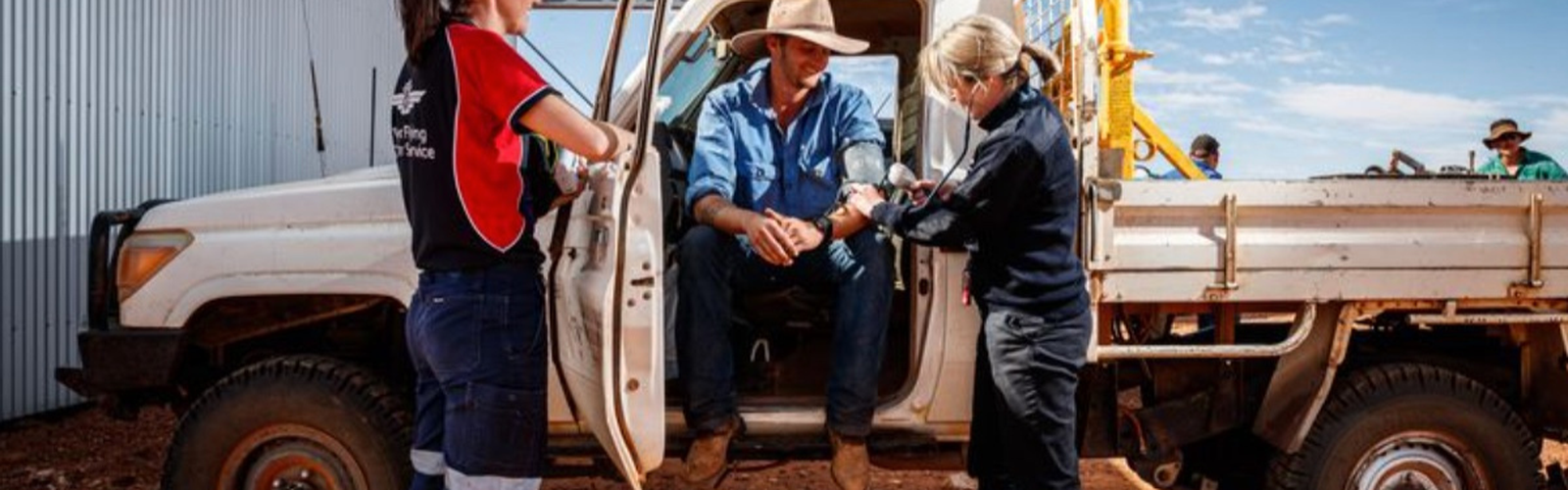 a nurse in an RFDS shirt and a doctor checking the heart rate of a patient who is sitting in a ute
