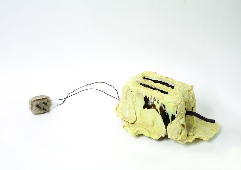 photo of a melted yellow looking toaster on a grey background.