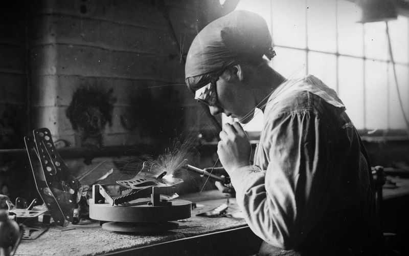 Vintage black and white photo of a woman welding metal components together.