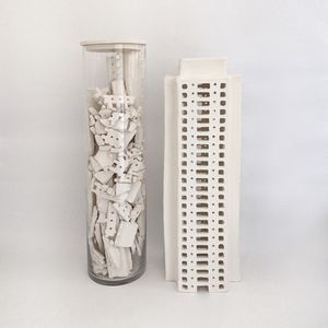 Photo of a building made in white clay next to a tall glass bottle with broken white clay pieces.