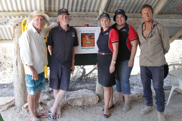 A group of people stand under a basic beach shelter. They are all smiling at the camera. 