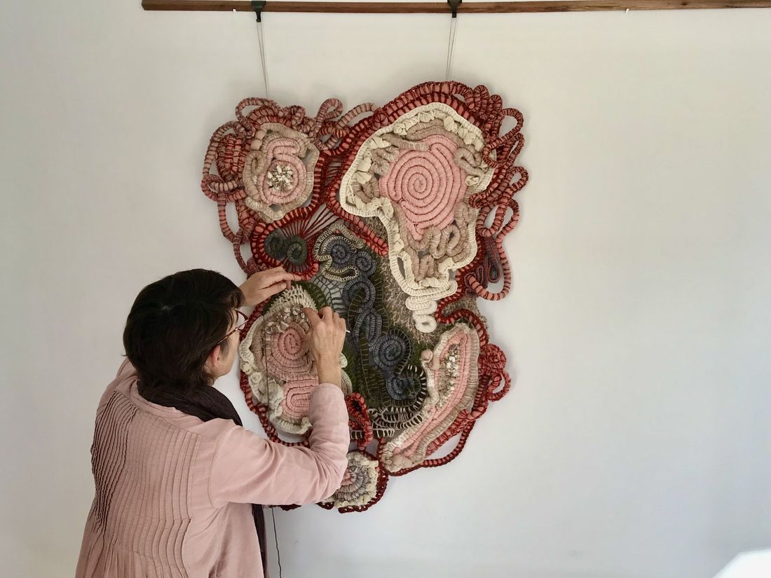 A photo of the back of Lynn Pavey working on her artwork Febrile Momentum, a coiled and woven vintage blanket work that takes the form the crusty clay pans of Kati Thanda