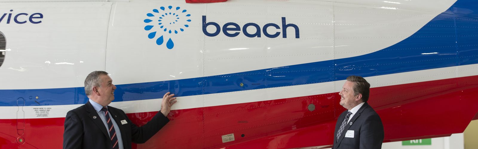 Two men in suits stand in front of an aircraft with a BEACH Energy logo on the side. The men are smiling. 