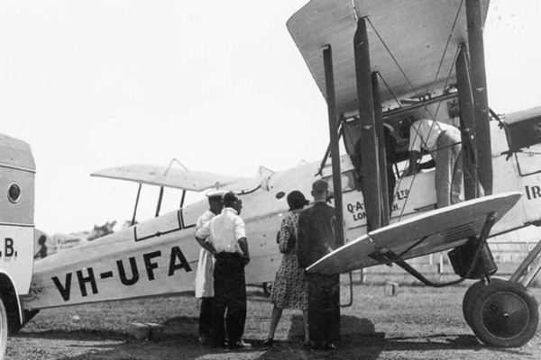 four people standing in front of a plane next to an ambulance, image is in black and white indicating it is from a long time ago