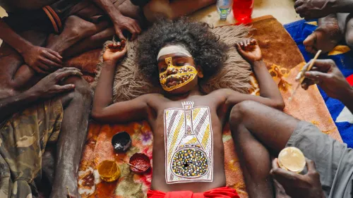 A child lays on the ground as surrounding people paint them