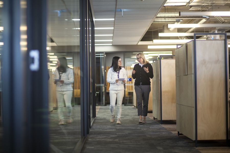 Two people walk towards the camera down an office hallway having a serious conversation