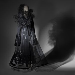 A mannequin wears a floor length, long sleeved black dress made from sheer fabric and shiny black pleather details