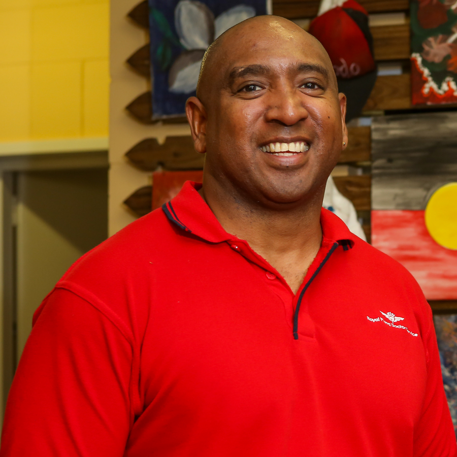 Joseph Oui is front and centre, he is wearing a bright red shirt with a white RFDS logo and is smiling widely.