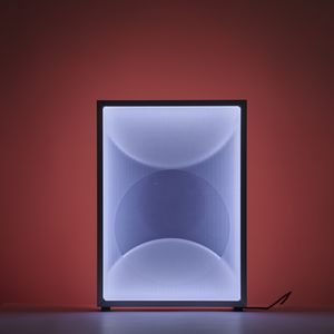 A square-shaped light is placed on a plinth, illuminating the surrounding area with a soft glow. The square light fixture projects blue and red tones with circular shapes.