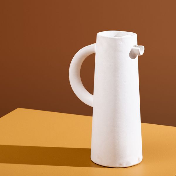 Photo of a tall white ceramic jug on a brown background
