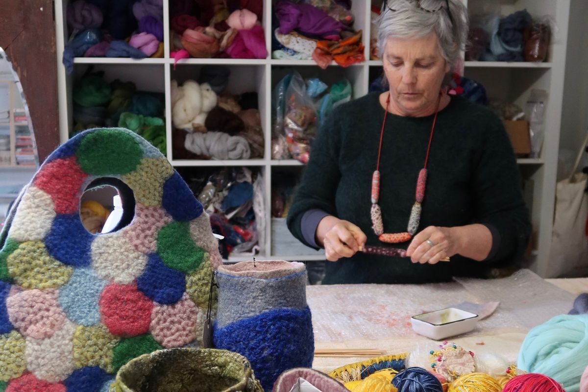 A portrait of fibre artist Gillian Brooks working in her studio at a table, with shelves full of felt in the background.