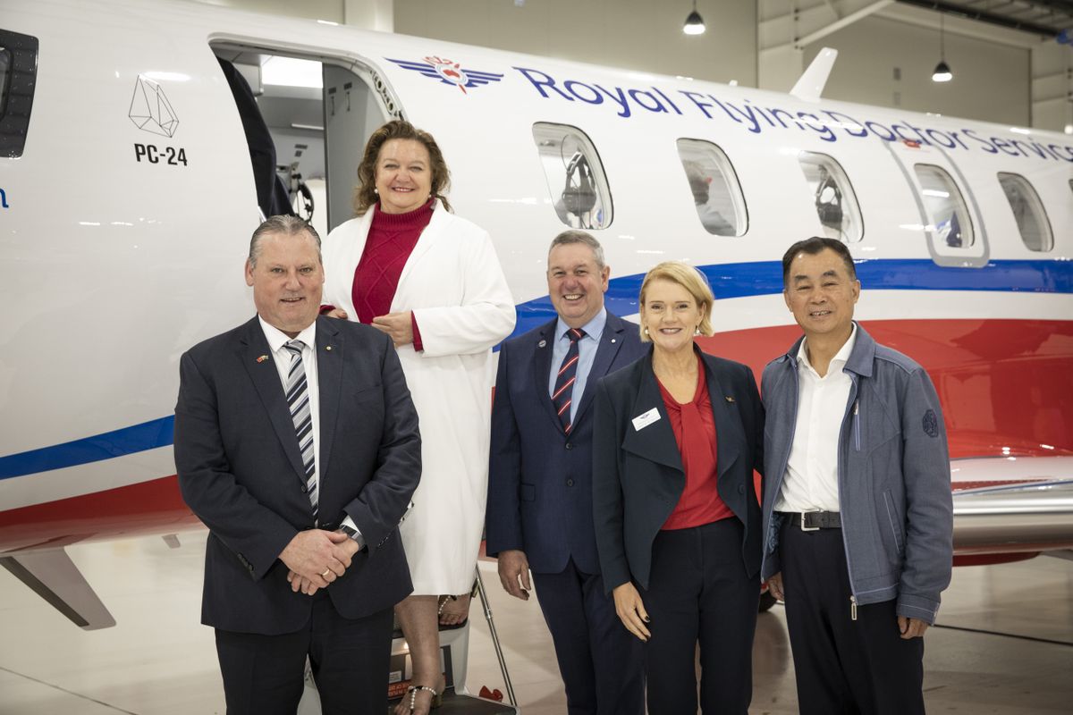 5 adults smile at the camera. They are all wearing corporate attires. An aircraft with RFDS logo and S Kidman and Co logo is behind them. 
