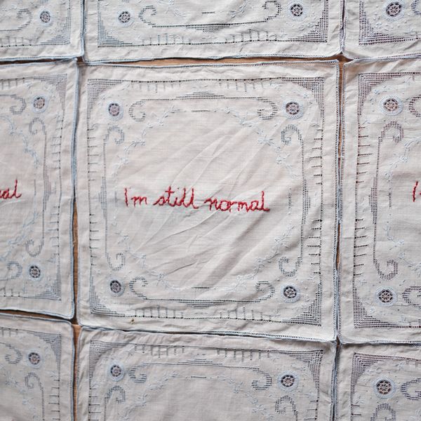A close up detail of a fine linen napkin embroidered with the statement, 'I'm still normal'