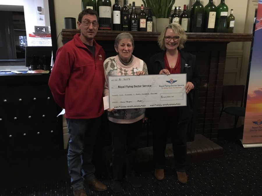 3 people smile at the camera. They are holding an oversized cheque for $140,000 made out to the RFDS. 