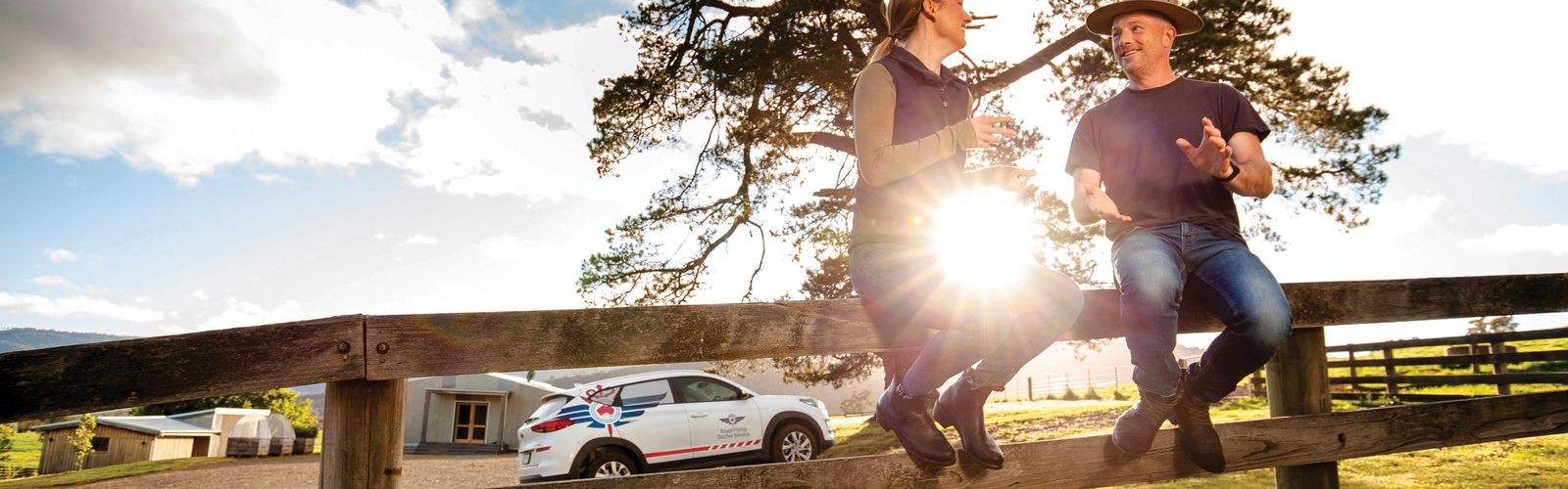 Two people sit on a fence talking