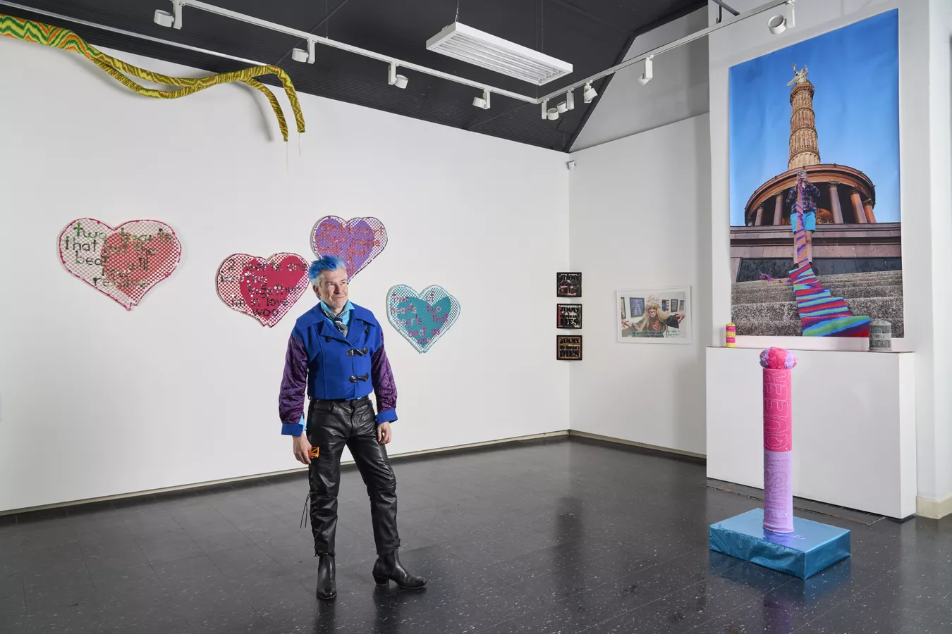 Troy-Anthony Baylis, stood in exhibition space with his works surrounding him.
