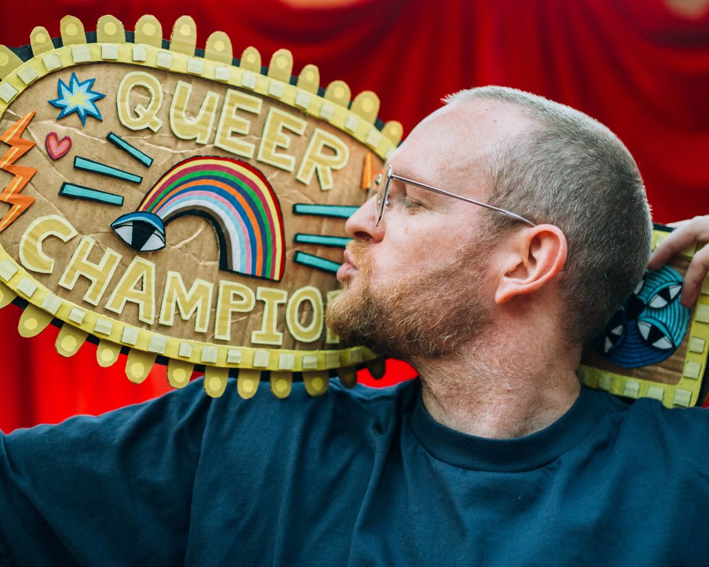 Photo of the artist kissing his 'Queer Champion' titled weight belt made from hand painted cardboard