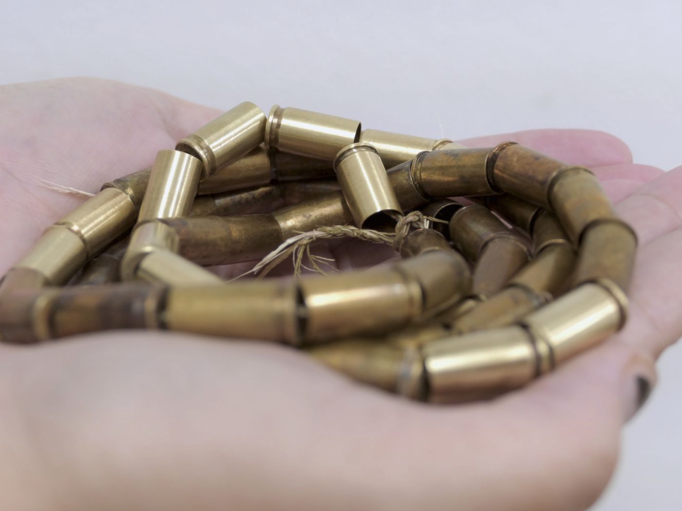 Artwork, bullet necklace on handcrafted twine, coiled and held in hands