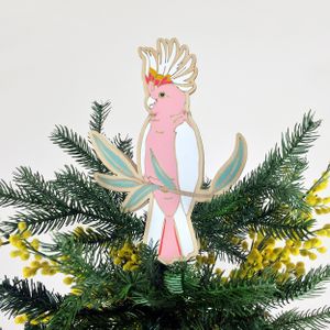 A hand-painted pink cockatoo ornament hanging from the top of a christmas tree