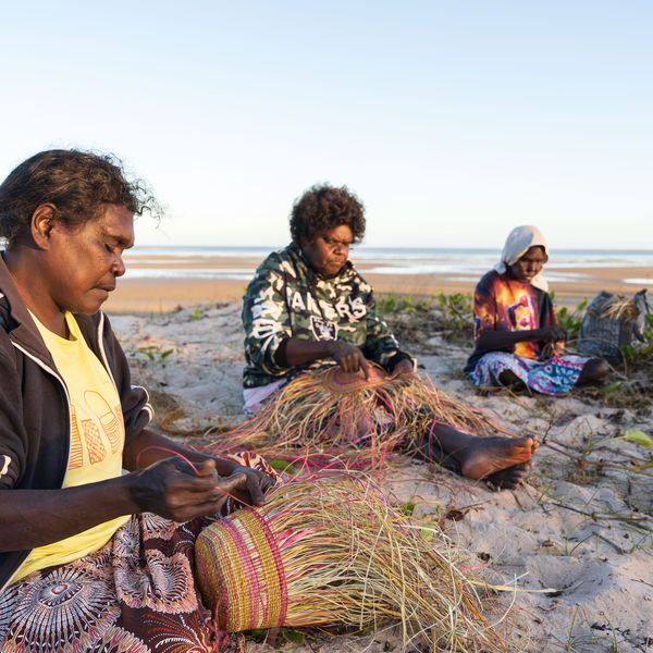 Four first nations women weaving baskets on the beach