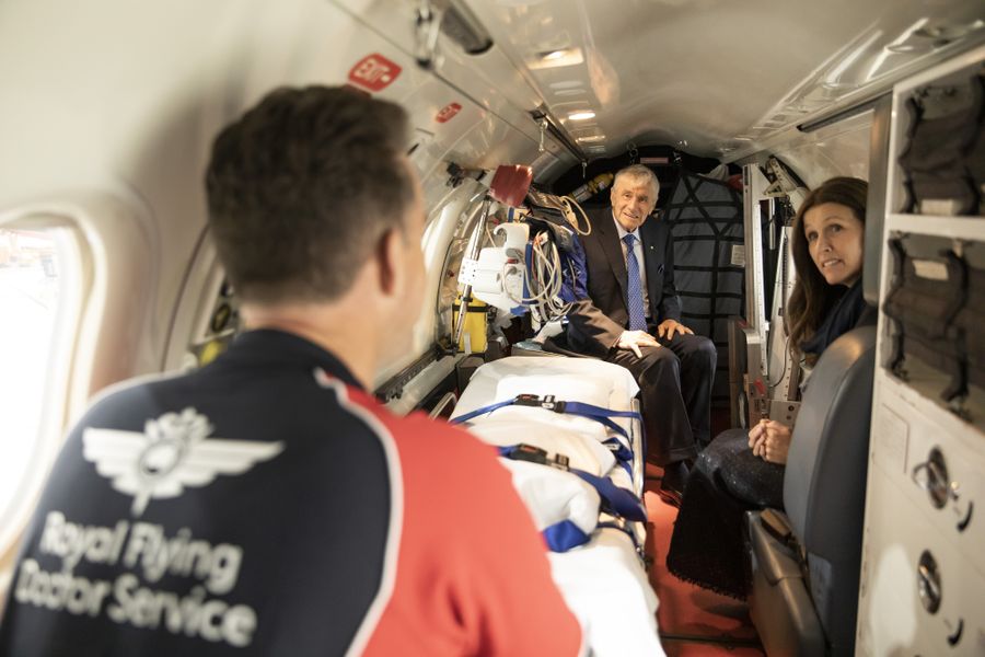 3 people sit inside a small aircraft with hospital stretcher. 