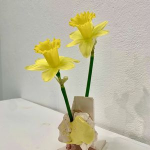 A photo of 2 daffodils in a vase made of broken pieces of ceramic, roughly glazed