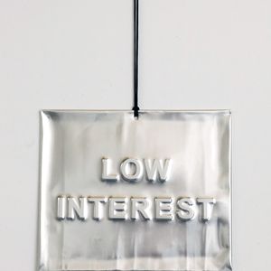 A rectangular silver sign with the text "LOW INTEREST" is hanging on a black cord against a white wall