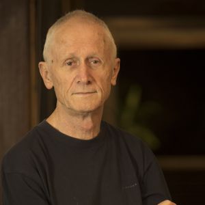 A portrait of ceramicist John Tuckwell with short white hair and a dark background behind him.