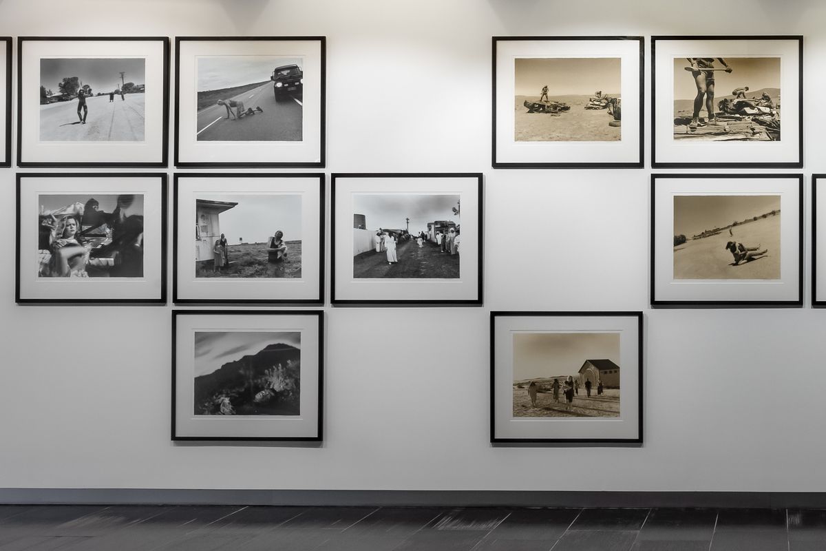 A white wall displays a grid of black and white and sepia photographs