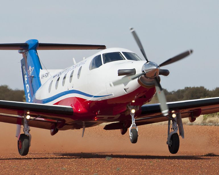 A RFDS propellor aircraft stands on red dirt. 
