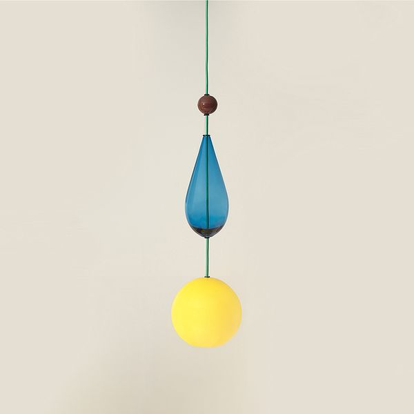 A pendant light made of glass shapes. From the top a brown glass sphere then blue drop shape and yellow sphere at base housing the globe