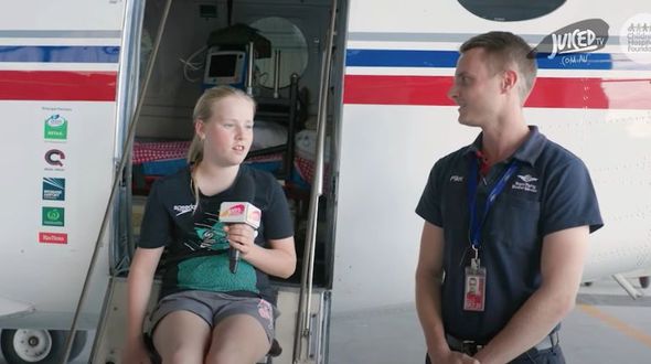 11 year old, Eliza, is pictured next to pilot, Elliot Johnston who is being interviewed. They are seated in front of an RFDS aeroplane, smiling.