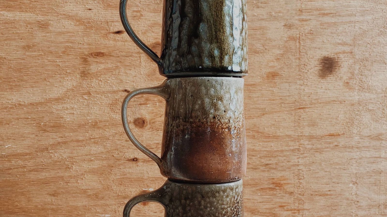 Bisque and glaze fired cups in various colours standing one on top of the other against a wood-ply background