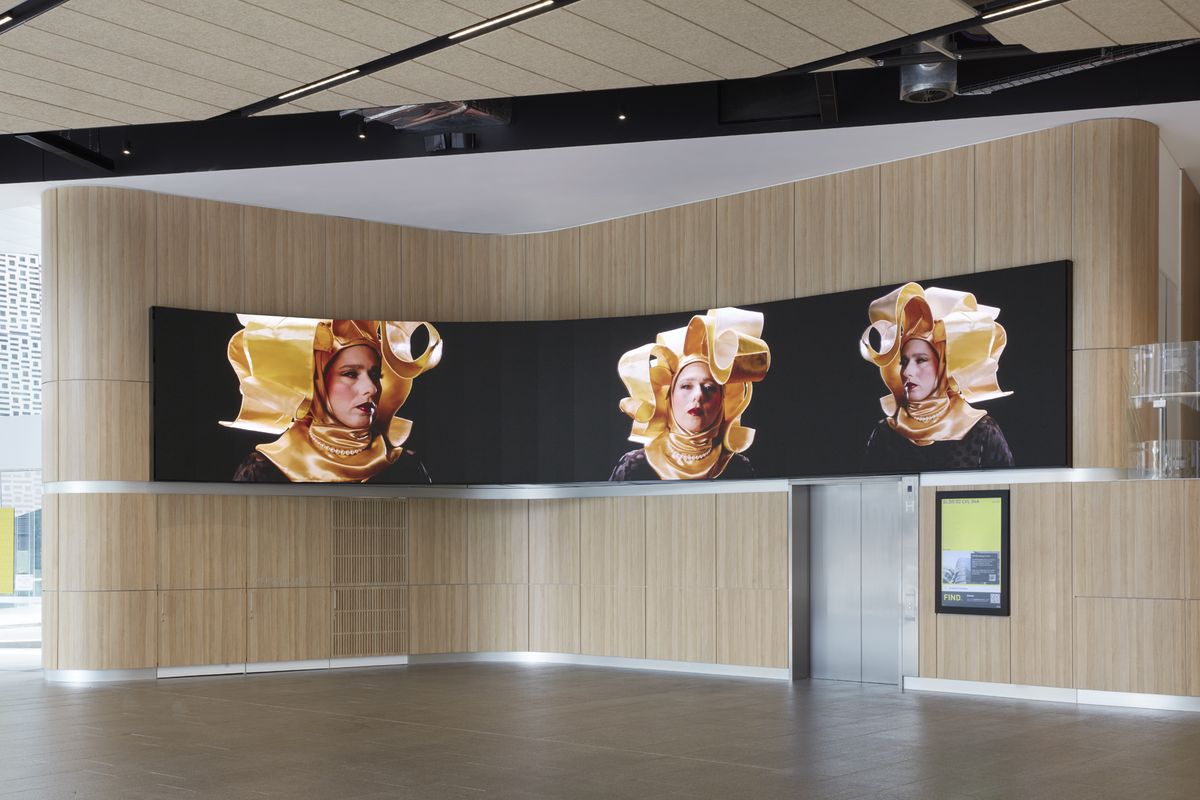 A photograph of a wide digital screen in a foyer with a woman in a headdress on the screen.