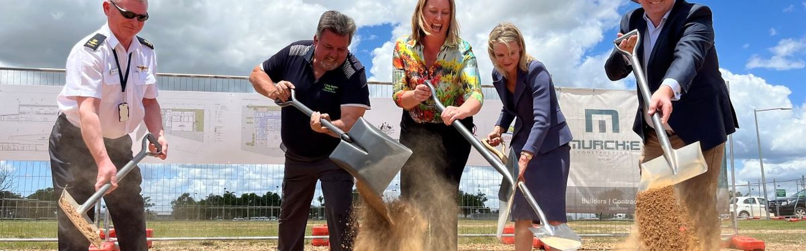 Five people using shovels dig up dirt on the site of the new aviation training facility.