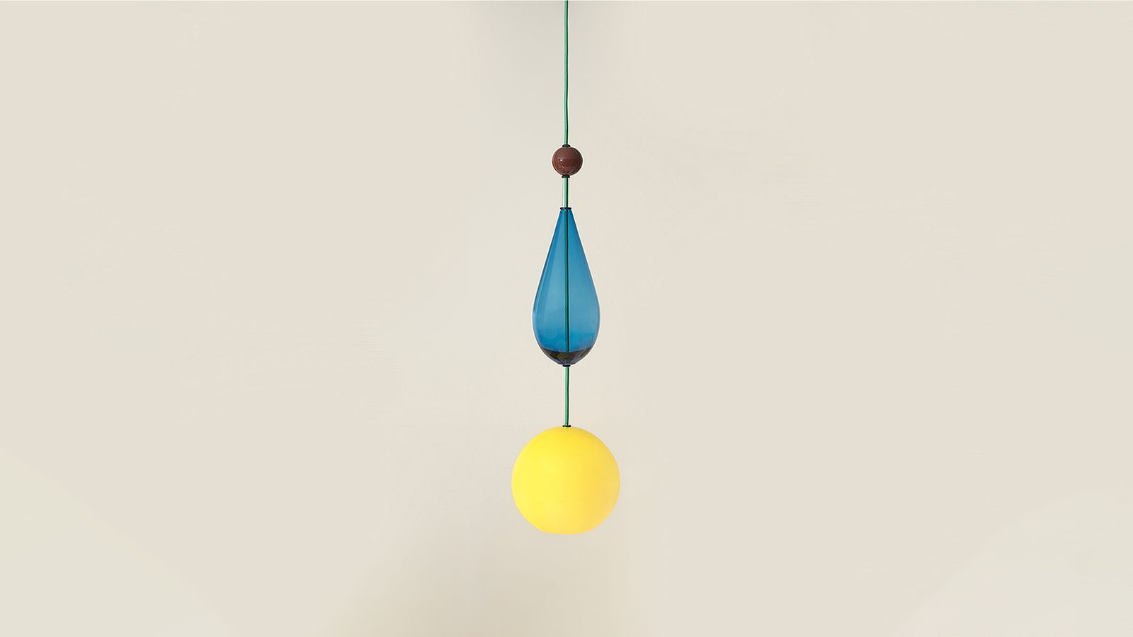 A pendant light made of glass shapes. From the top a brown glass sphere then blue drop shape and yellow sphere at base housing the globe