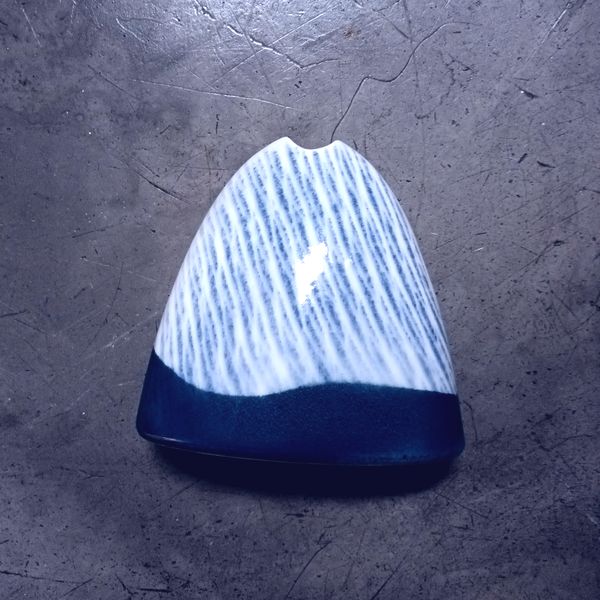 A blue and white triangular shaped ceramic vase on a grey background