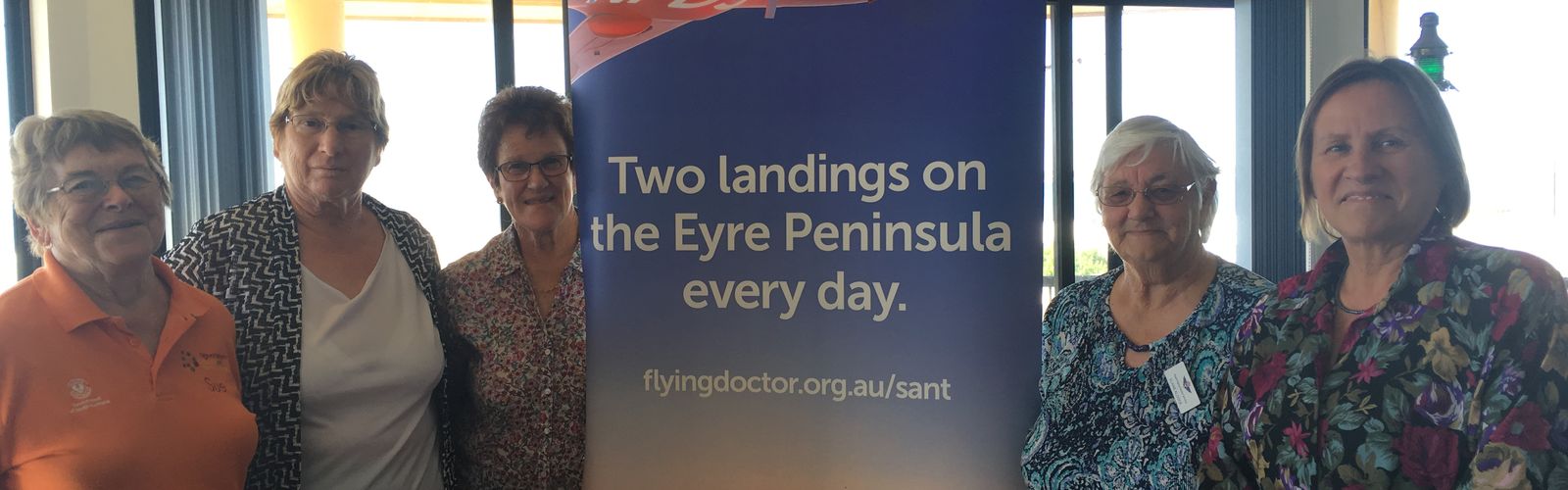 Four women smile at the camera. They are holding an oversized cheque made out to the RFDS for $20,000. 