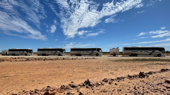 Four Kangaroo Bus Line busses covered in dust on a dirt road