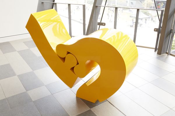 A photo of a yellow sculpture with to interlocking parts in front of a window