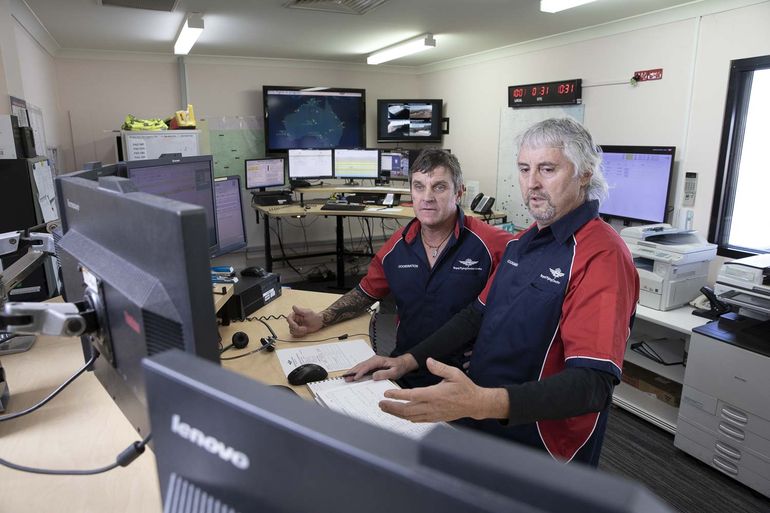 Two men in RFDS uniform look seriously at a computer screen. 