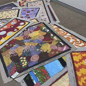 A photo of a pile of canvas on the ground with beautiful finished artworks on them.