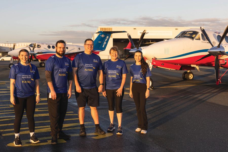 Five RFDS Oceans to Outback fundraising participants wearing 'Keeping the Flying Doctor Flying' t-shirts, standing on the tarmac at sunset.