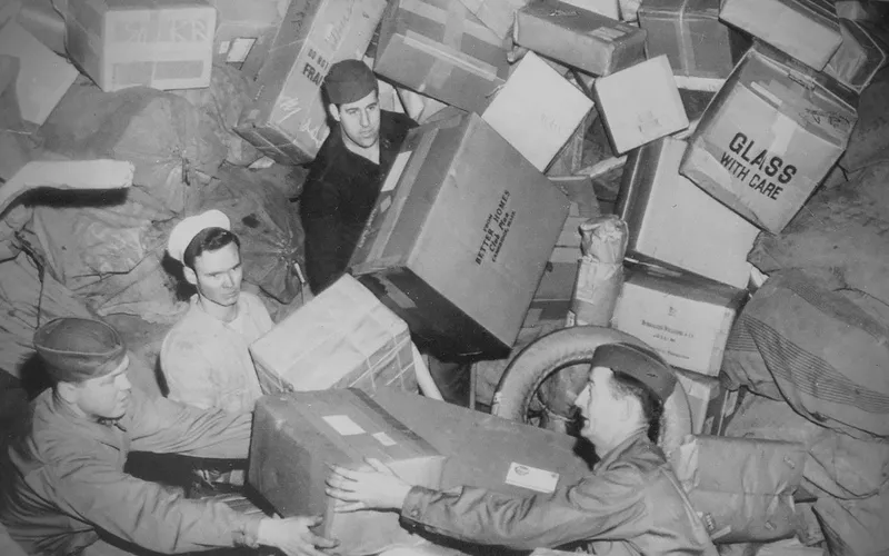 Three U.S. soldiers being almost buried by parcels at a mail depot during World War 2, circa 1944